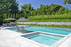 an empty swimming pool with lounge chairs and umbrellas in the background, surrounded by greenery