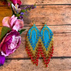 a pair of beaded earrings sitting on top of a wooden table next to flowers