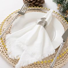 a place setting with white napkins, silverware and pine cone decorations on the table