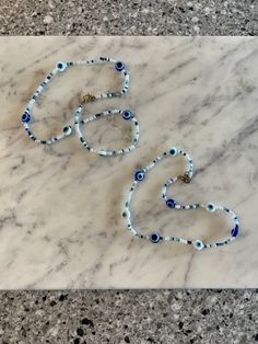 2 chokers beaded by hand! blue and white evil eye beads with a mixture of white, blue, and clear beads! along with mini white pearls! they are both adjustable! 2 measurements available- 12 inches, and 15 inches! please reach out about any questions! check my shop for customizable evil eye waist beads in 8 colors and customizable in over 50 ways! this product ships same day or next day! Bohemian White Beaded Necklace With Evil Eye, White Bohemian Beaded Necklace With Evil Eye, Adjustable White Beaded Necklace With Evil Eye, White Evil Eye Beaded Bracelets For Festivals, Blue Evil Eye Bracelet With Round Beads For Festivals, White Evil Eye Bracelet With Tiny Round Beads, White Evil Eye Jewelry For Festivals, Blue Beaded Necklaces With Letter Beads For Festivals, Blue Beaded Necklace With Letter Beads For Festival