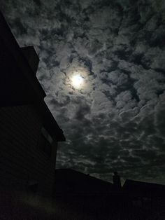 the full moon shines brightly in the dark sky above some houses on a cloudy night