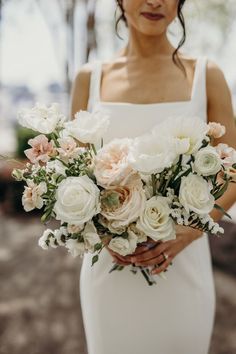 a woman holding a bouquet of white and pink flowers on her wedding day in front of trees