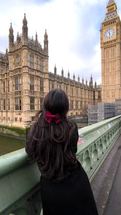 a woman is standing on a bridge looking at the clock tower in london, england