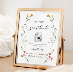 a photo frame with flowers on it sitting next to a white flower arrangement and a vase