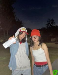 two young women standing next to each other in front of a dark sky at night