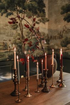 candles are lined up on a table in front of a wall with a painting behind it