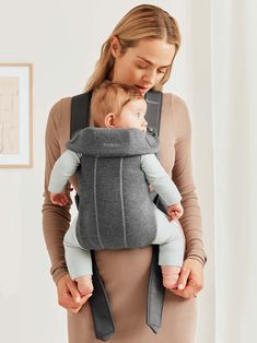 a woman holding a baby in a grey carrier