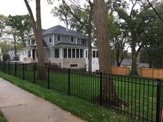 a black fence in front of a house with trees on the side walk and green grass