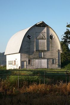 an old barn sits in the middle of a field