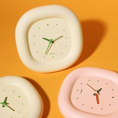 three small clocks sitting on top of a yellow and pink surface with one clock in the middle