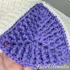 a hand holding a purple and white crocheted object