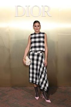 a woman standing in front of a sign wearing black and white checkered dress with pink heels