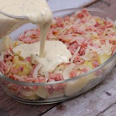 a bowl filled with food and dressing being poured into it's side dish on top of a wooden table