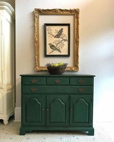 a green dresser with a painting on the wall above it and a basket of flowers sitting on top