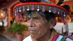 an old man wearing a hat with feathers and beads on it's head is looking at the camera