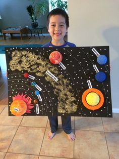 a young boy is holding up a solar system art project that includes the sun, planets and stars