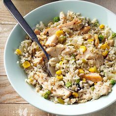 a white bowl filled with rice and vegetables next to a spoon on top of a wooden table