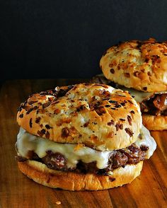 two hamburgers sitting on top of a wooden table covered in cheese and meat toppings