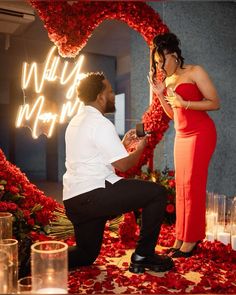 a man kneeling down next to a woman in front of a heart - shaped sign