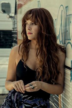 a woman with long hair leaning against a wall