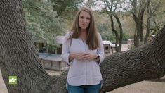 a woman standing in front of a tree with her hands folded up and looking at the camera