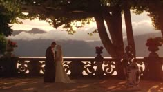 a bride and groom standing next to each other in front of trees with mountains in the background