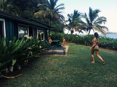 two women are playing with a frisbee in the grass near some water and palm trees