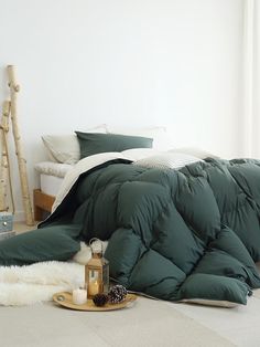 an unmade bed with green comforter and pillows on the floor next to it