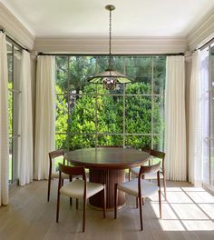 a dining room table and chairs in front of a large window with white drapes