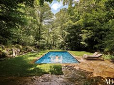 an outdoor swimming pool surrounded by lush green trees and lawn furniture with lounge chairs around it