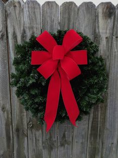 a wreath with a red bow hanging on a wooden fence