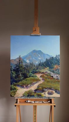 an easel with a painting on top of it and a mountain in the background