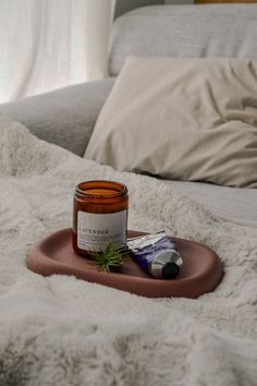 a candle on a tray next to a bottle of essentials sitting on a bed