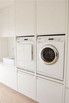 a washer and dryer in a white laundry room with wood flooring on the side