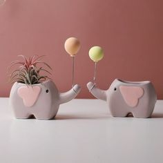 two elephant planters with air plants in them, one holding a balloon and the other holding a ball