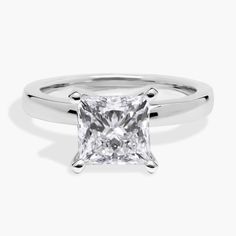 a princess cut diamond engagement ring on a white background, with the center stone set in 18k white gold