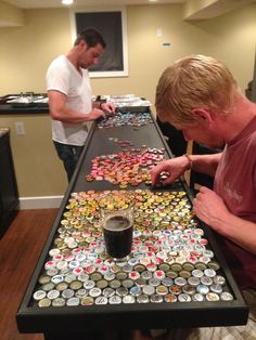 two men standing at a table covered in beer caps