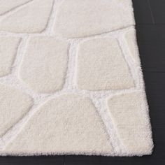 a white area rug with squares and rectangles on the floor in front of a black background