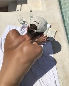 a shirtless man laying on top of a white towel next to a swimming pool