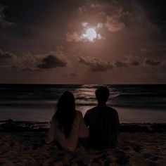 two people sitting on the beach watching the sun set