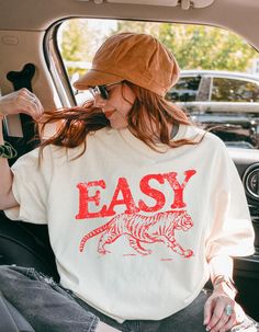 Add some retro vibes to your wardrobe with our vintage-inspired "Easy Tiger" graphic t-shirt! This trendy tee features a bold tiger design with a throwback to 70s vintage style, perfect for casual outfits, festival looks, or laid-back weekends. Made from soft, high-quality fabric, it offers both comfort and style, making it your go-to statement piece. Pair it with jeans, shorts, or a jacket for an effortlessly cool look. Available in a variety of sizes and colors, this graphic tee is perfect for Retro Slogan Tops, Retro Letter Print T-shirt For Everyday, Retro Text Print T-shirt For Everyday, Trendy T-shirt With Vintage Print And Relaxed Fit, Retro Text Print T-shirt, Vintage Letter Print T-shirt For Everyday, Vintage Everyday T-shirt With Screen Print, Retro Pre-shrunk T-shirt For Everyday, Vintage Pre-shrunk T-shirt For Everyday