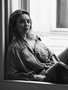 a black and white photo of a woman sitting on a window sill