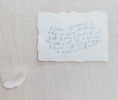 a piece of paper with writing on it next to a white flower and a feather