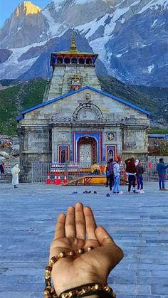 a person holding their hand up in front of a building with mountains in the background