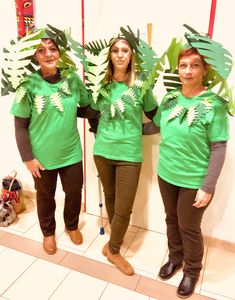 three people in green shirts standing next to each other with leaves on their shoulders and arms