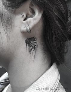 a woman's ear has a black feather tattoo on it