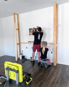 two people are doing construction work on a wall in an unfinished room with hard wood flooring