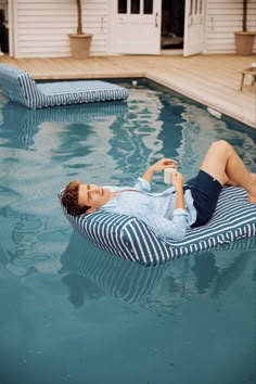 a woman laying on top of a blue and white striped pillow in a swimming pool