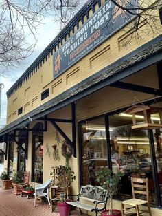 a store front with benches and potted plants outside