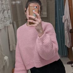 a woman taking a selfie in front of a mirror wearing a pink sweater and black pants